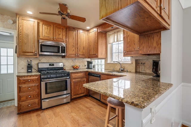 kitchen with light stone counters, appliances with stainless steel finishes, a breakfast bar, and kitchen peninsula