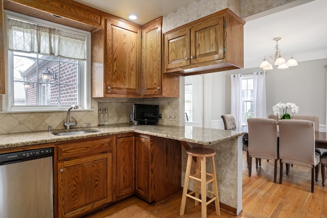 kitchen featuring sink, light hardwood / wood-style floors, dishwasher, and light stone countertops