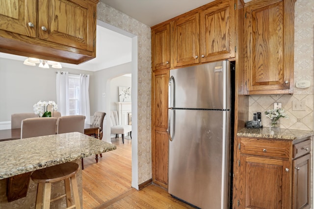 kitchen featuring light stone counters, stainless steel fridge, light hardwood / wood-style floors, and tasteful backsplash