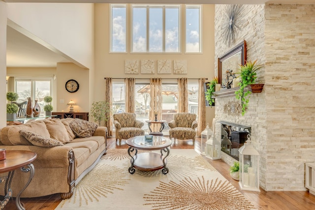 living room with a towering ceiling, a stone fireplace, and light wood-type flooring