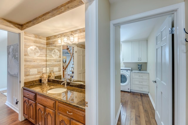 bathroom featuring hardwood / wood-style flooring, wooden walls, vanity, and washer / clothes dryer