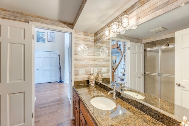 bathroom featuring vanity, hardwood / wood-style flooring, a shower with shower door, and wood walls