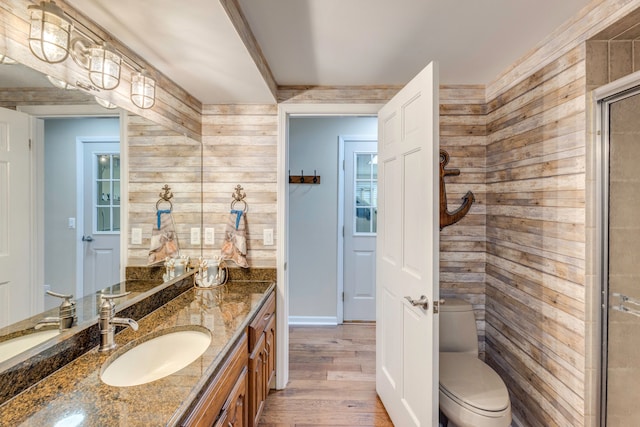 bathroom with wood walls, wood-type flooring, vanity, toilet, and a shower with door