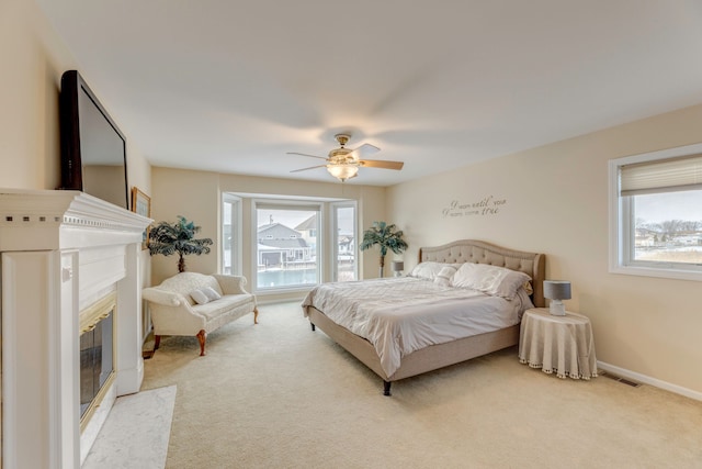 bedroom featuring multiple windows, a fireplace, light colored carpet, and ceiling fan