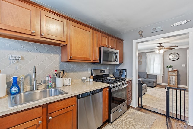 kitchen with sink, decorative backsplash, ceiling fan, stainless steel appliances, and light wood-type flooring