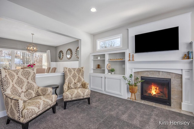 sitting room featuring a tiled fireplace, a notable chandelier, carpet floors, and a healthy amount of sunlight