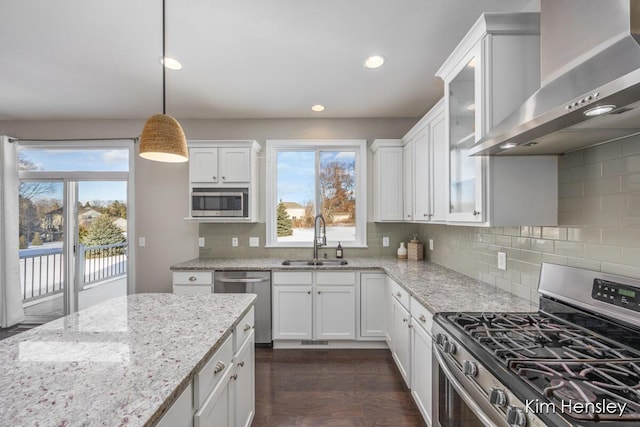 kitchen featuring decorative light fixtures, sink, white cabinets, stainless steel appliances, and wall chimney exhaust hood