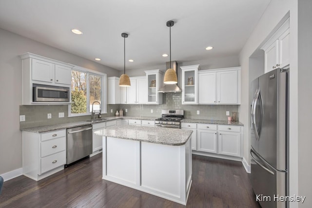 kitchen featuring wall chimney exhaust hood, white cabinetry, a kitchen island, pendant lighting, and stainless steel appliances