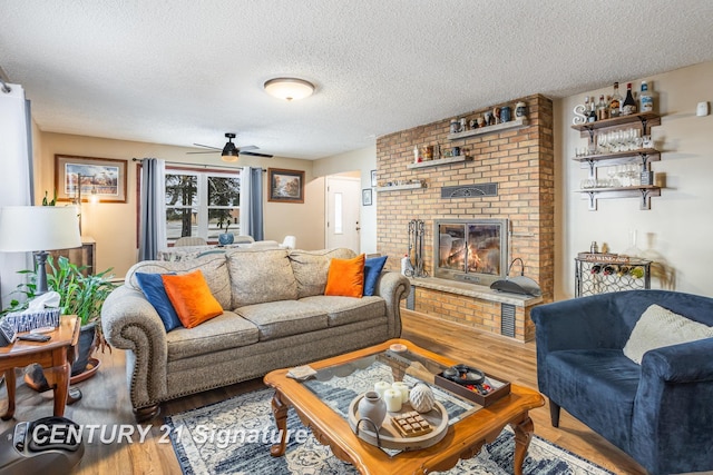 living room featuring hardwood / wood-style flooring, ceiling fan, a brick fireplace, and a textured ceiling