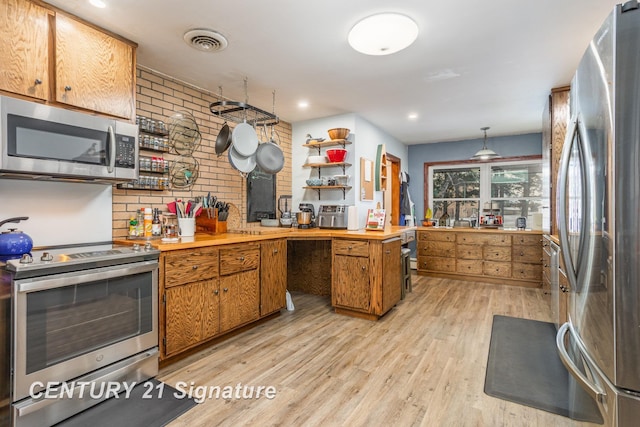 kitchen featuring stainless steel appliances, brick wall, hanging light fixtures, and light wood-type flooring