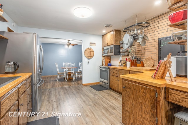 kitchen with ceiling fan, stainless steel appliances, light hardwood / wood-style floors, brick wall, and wood counters