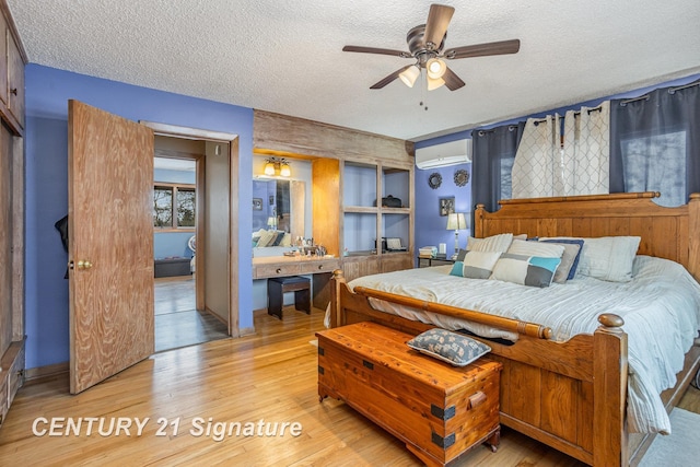 bedroom with ceiling fan, a wall unit AC, a textured ceiling, and light wood-type flooring