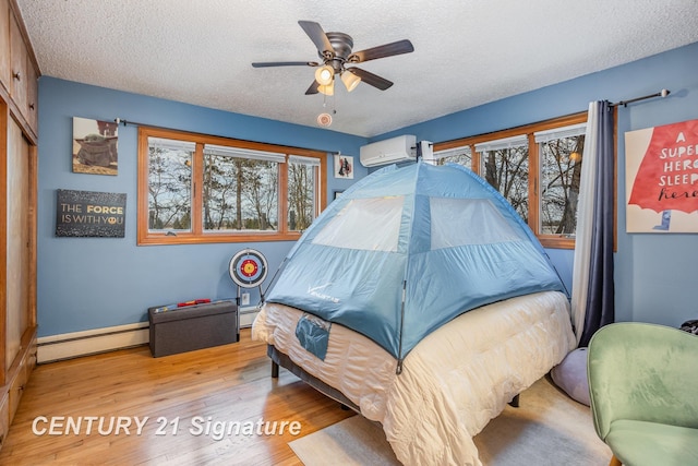 bedroom with a wall mounted AC, a textured ceiling, light wood-type flooring, baseboard heating, and ceiling fan