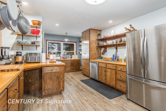 kitchen featuring pendant lighting, sink, light hardwood / wood-style flooring, appliances with stainless steel finishes, and butcher block counters