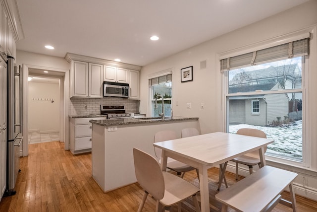 kitchen with sink, dark stone countertops, stainless steel appliances, white cabinets, and kitchen peninsula