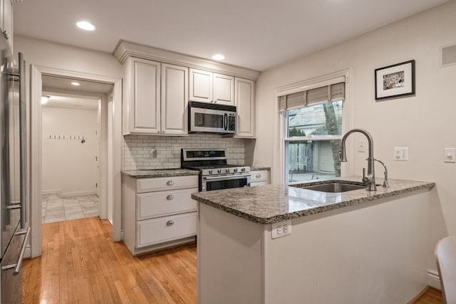 kitchen with sink, appliances with stainless steel finishes, white cabinetry, kitchen peninsula, and dark stone counters