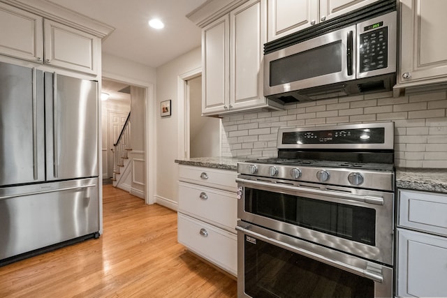 kitchen featuring stainless steel appliances, tasteful backsplash, light stone countertops, and light wood-type flooring