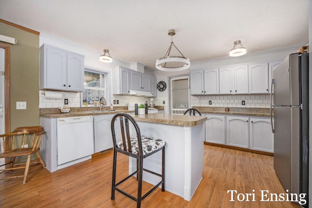 kitchen with white cabinetry, a center island, a kitchen breakfast bar, stainless steel fridge, and white dishwasher