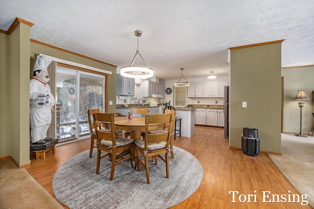 dining space featuring ornamental molding, sink, a textured ceiling, and light hardwood / wood-style floors
