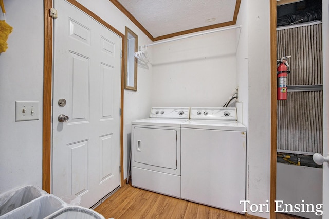 laundry area featuring ornamental molding, washing machine and dryer, light hardwood / wood-style flooring, and a textured ceiling