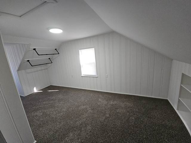 additional living space with dark colored carpet and vaulted ceiling