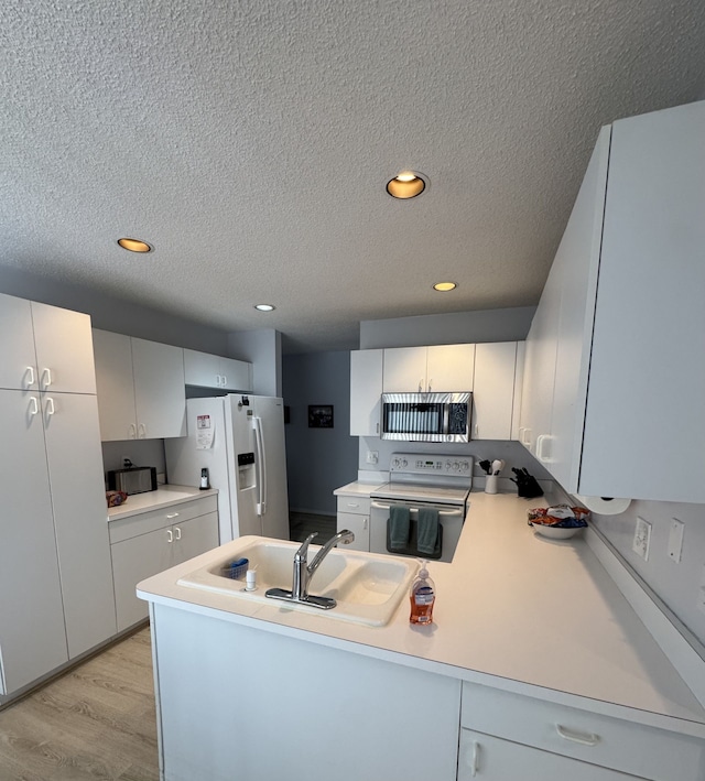 kitchen with white appliances, a peninsula, light countertops, light wood-style floors, and a sink