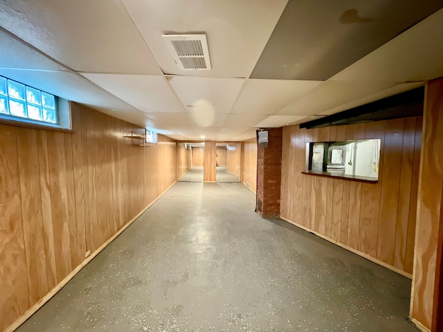 basement with a paneled ceiling and wood walls