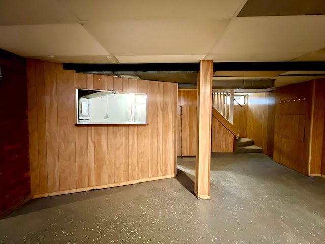 basement with a drop ceiling and wood walls