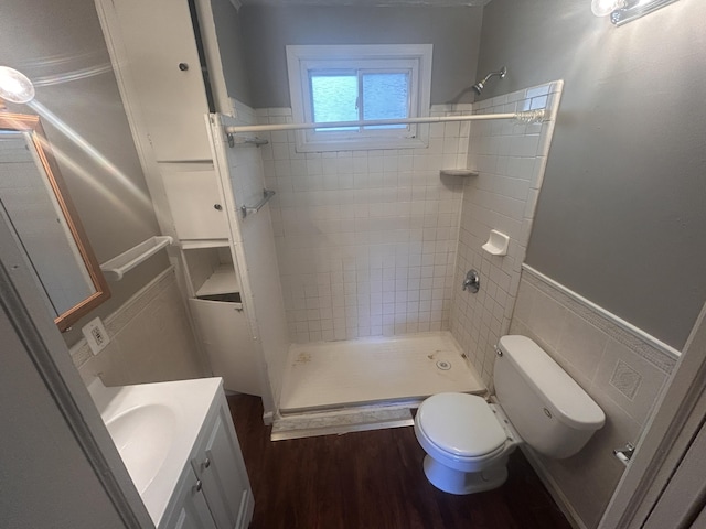 bathroom featuring tile walls, hardwood / wood-style flooring, vanity, tiled shower, and toilet