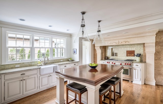 kitchen with sink, light hardwood / wood-style flooring, a breakfast bar, designer range, and decorative light fixtures