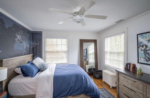 bedroom with multiple windows, crown molding, radiator heating unit, and hardwood / wood-style flooring