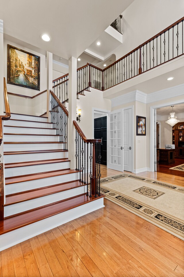 stairway with hardwood / wood-style flooring, a towering ceiling, crown molding, and a notable chandelier