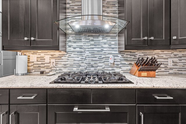 kitchen with light stone counters, island exhaust hood, stainless steel gas stovetop, and backsplash