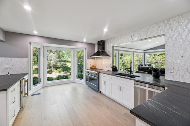 kitchen featuring a wealth of natural light, white cabinetry, stainless steel appliances, light wood-type flooring, and wall chimney exhaust hood