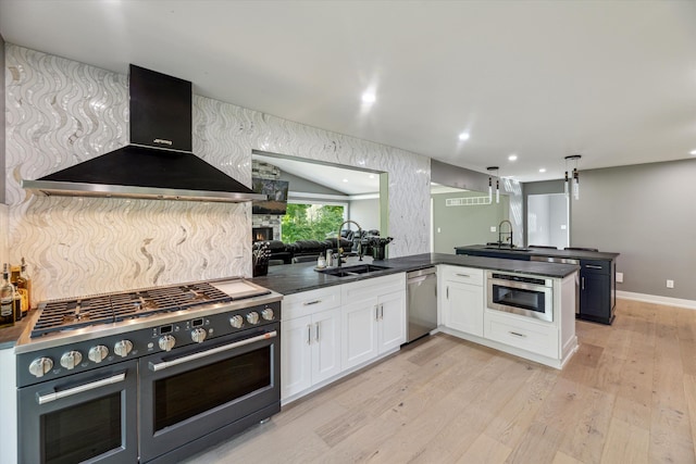 kitchen with wall chimney range hood, sink, appliances with stainless steel finishes, white cabinets, and kitchen peninsula