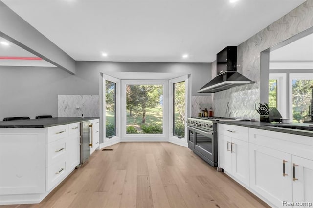 kitchen with white cabinets, decorative backsplash, wall chimney exhaust hood, and range with two ovens