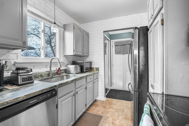 kitchen featuring sink, gray cabinetry, hanging light fixtures, appliances with stainless steel finishes, and brick wall