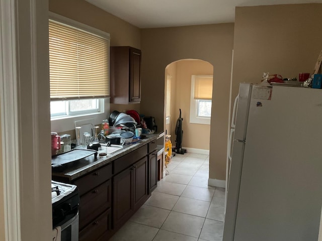 kitchen with a wealth of natural light, white fridge, stove, light tile patterned floors, and dark brown cabinets