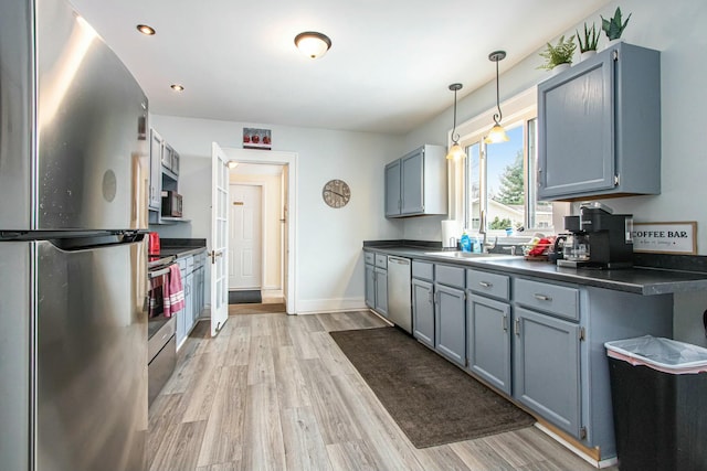 kitchen featuring pendant lighting, sink, blue cabinetry, stainless steel appliances, and light wood-type flooring