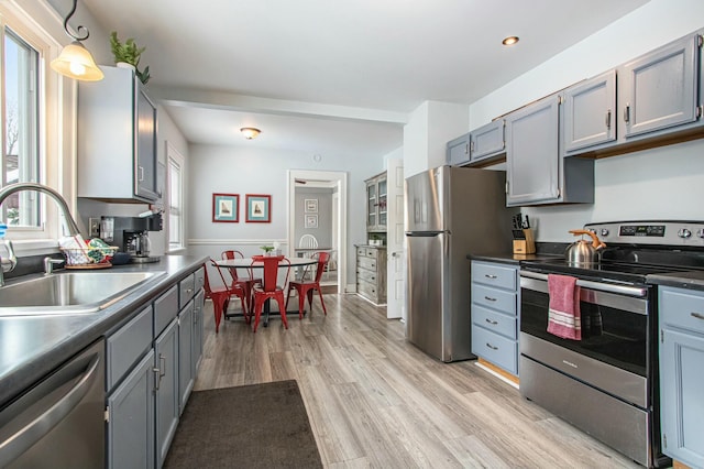 kitchen featuring sink, gray cabinets, appliances with stainless steel finishes, light hardwood / wood-style floors, and decorative light fixtures