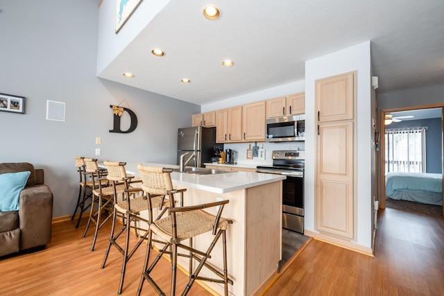 kitchen featuring a breakfast bar area, light brown cabinets, a sink, light countertops, and appliances with stainless steel finishes