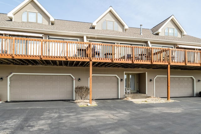 back of property featuring driveway, an attached garage, and a shingled roof