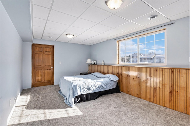 bedroom with a paneled ceiling, carpet floors, and wood walls