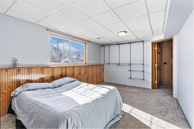 bedroom with carpet floors, a paneled ceiling, and wood walls