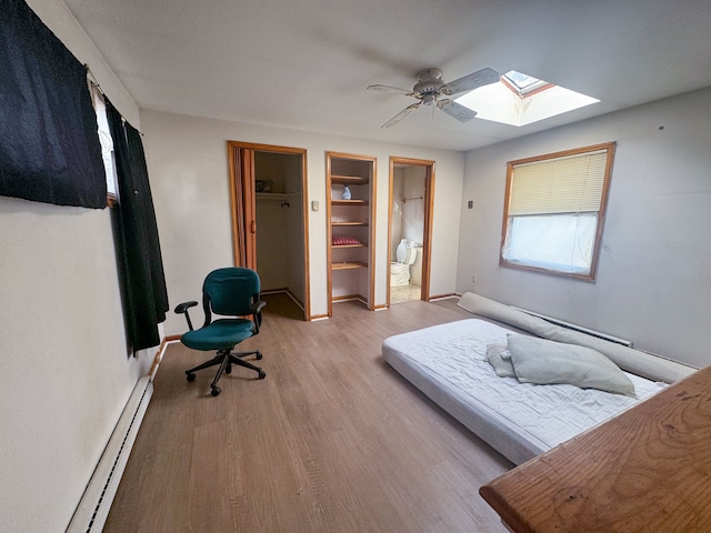 bedroom with a skylight, light hardwood / wood-style floors, ceiling fan, and baseboard heating