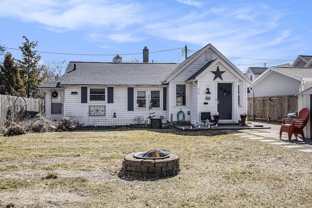 view of front of property with a shingled roof, a fire pit, a front yard, and fence