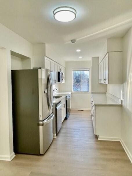 kitchen with stainless steel appliances, white cabinetry, and light hardwood / wood-style floors