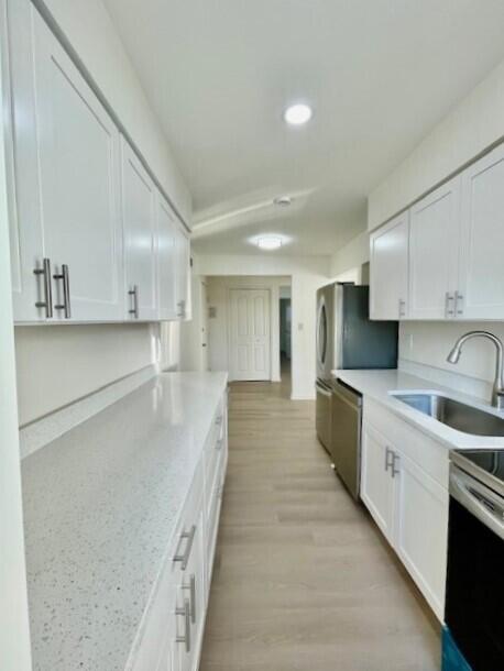 kitchen with light wood-type flooring, stainless steel dishwasher, sink, and white cabinets