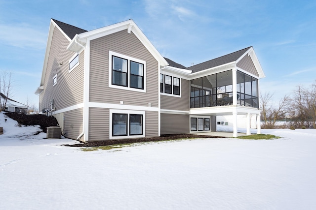 snow covered house featuring a sunroom and central air condition unit