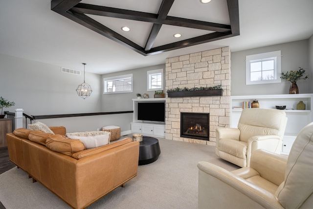 living room with plenty of natural light, beam ceiling, a stone fireplace, and a notable chandelier